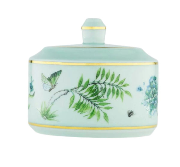 A charming piece resembling the Aquazzura Casa Secret Garden Sugar Bowl—a small, round, light green porcelain container with a lid, decorated with floral and butterfly designs, and gold trim accents.