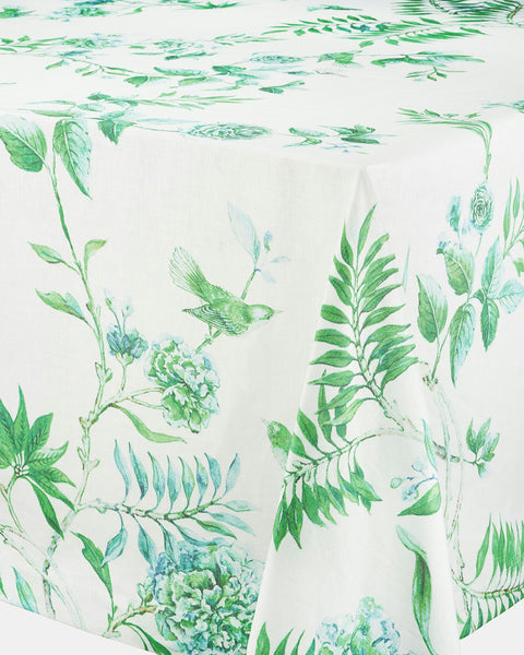 A table adorned with the high-quality Aquazzura Secret Garden Tablecloth from Aquazzura Casa, showcasing a white linen base with green botanical and bird prints.