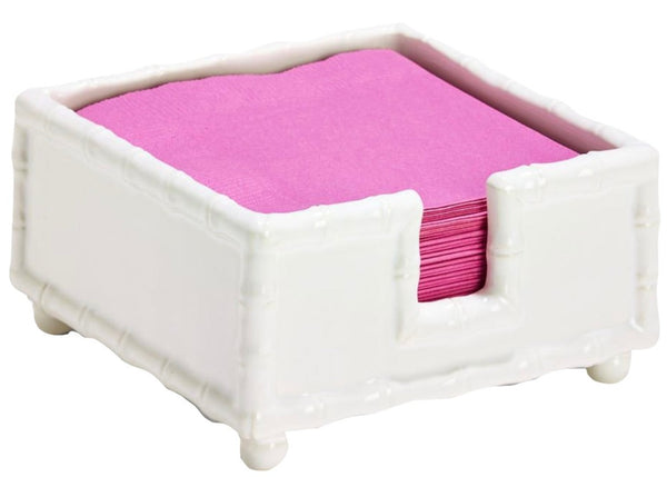 A white glazed ceramic Two's Company Hampton Faux Bamboo napkin holder containing pink paper napkins.