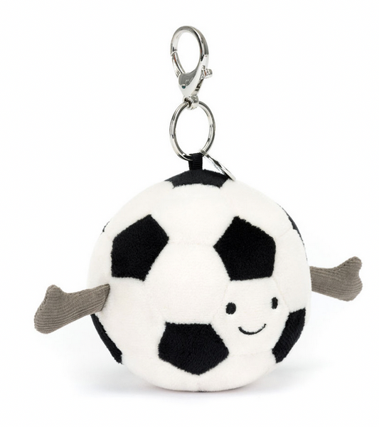 A small plush keychain designed as a smiling soccer ball with black and white patches, featuring two gray fabric arms and a metal clasp on top. Perfect as a Jellycat Amuseables Sports Soccer Bag Charm for any soccer fan gift, it also includes an official Jellycat tag.