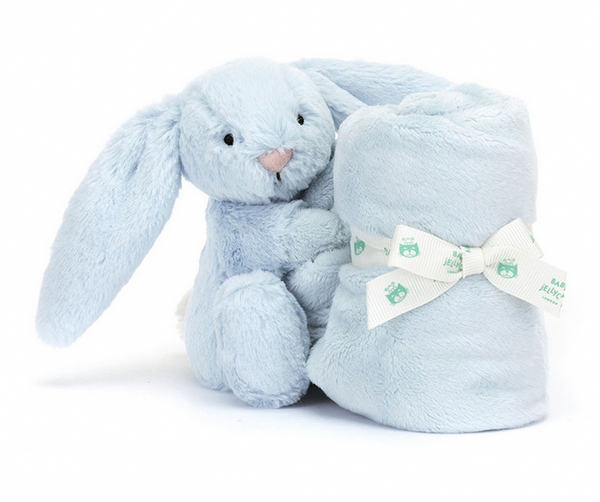 A Jellycat Bashful Blue Bunny Soother sits next to a rolled, light blue soft blanket secured with a white ribbon featuring small green bear designs. This delightful newborn gift is crafted from recycled fibers, making it both adorable and eco-friendly.