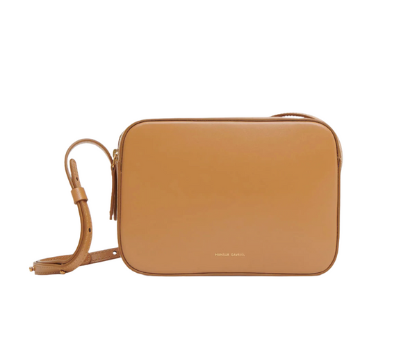 A Mansur Gavriel Camera Bag, a rectangular beige Italian Spazzolato Leather crossbody bag with an adjustable strap and a small gold logo in the bottom center, reads "MANSUR GAVRIEL.