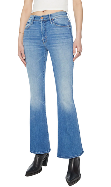 Individual wearing Mother The Weekender jeans in mid-blue wash with a mid-rise flare, paired with a white top and black heeled boots, standing against a white background.