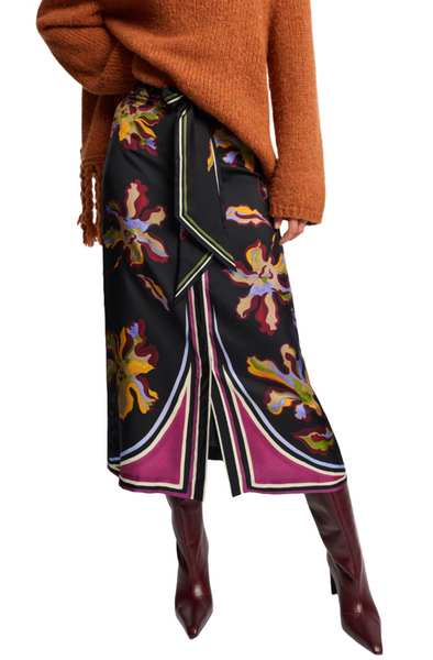 A person wearing a burnt orange sweater, the Dorothee Schumacher Floral Seductive Skirt by Dorothee Schumacher—a black floral-patterned silk twill skirt with a center front button placket and slit—and burgundy knee-high boots.