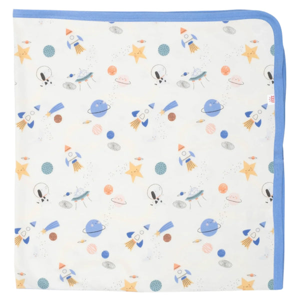 The Magnetic Me Stellar Tails Blanket by Magnetic Me is a white baby blanket with blue trim, adorned with repeated illustrations of rockets, planets, stars, and astronauts. It is made from eco-friendly TENCEL modal for a soft touch.