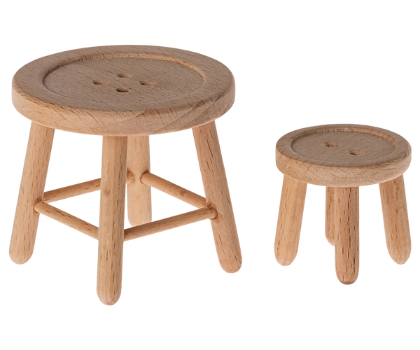 Two small, round, wooden stools from the Maileg Table and Stool Set, Mouse by Maileg feature button-like tops. The larger stool boasts a cross-braced base, while the smaller stool showcases a simpler design. These charming pieces resemble mouse furniture perfect for a Mouse Hole Farmhouse.