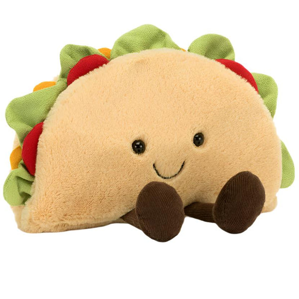 Introducing the Jellycat Amuseables Taco by Jellycat: a plush toy designed to resemble a taco, complete with a smiling face and small legs. This adorable toy features decorative toppings like lettuce, tomato, and cheese, all nestled within its soft taco shell.