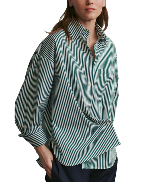 A person is wearing a loose-fitting, green and white striped TWP New Earl Shirt by TWP with long sleeves and a collar. The bold striped cotton shirt is tucked into dark trousers.