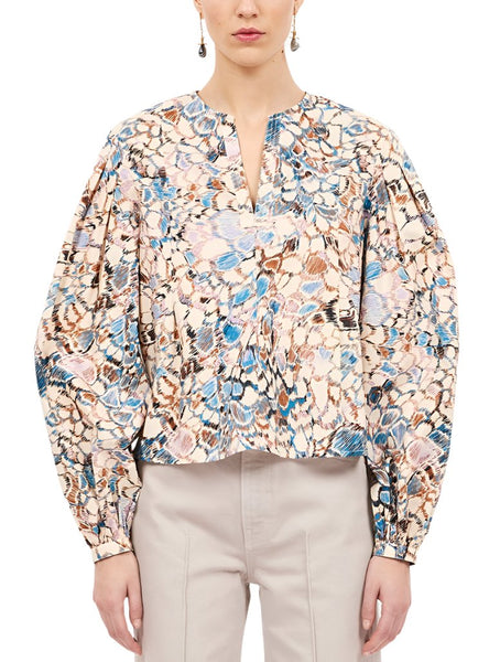 A person wearing the Ulla Johnson Ilara Blouse, which features a feathered print, V-neckline, and long, full sleeves, paired with light-colored pants.