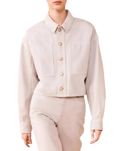 A person wearing a light beige collared shirt and matching pants, with the shirt featuring a button-down front and chest pockets, evokes the sleek elegance of the Ulla Johnson The Bobbi Denim Jacket.