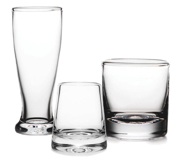 Three empty glass cups from the Simon Pearce Ascutney Collection—a tall, narrow one; a short, wide Irish whiskey glass; and a medium cylindrical one—sit side by side on a white surface. This handmade set by Simon Pearce blends elegance with functionality.