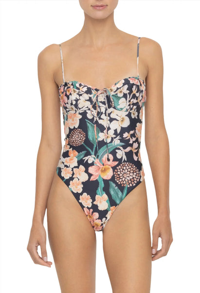 A person wearing the Agua By Aguabendita Ebano One Piece, a floral swimsuit featuring adjustable straps and a front tie detail, crafted from recycled polyester.