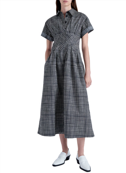 A person wearing a Proenza Schouler Balston Grid Poplin Dress by Proenza Schouler. The dress has a fitted top, a flared skirt with pockets, and point collar detailing. They are also wearing white shoes.