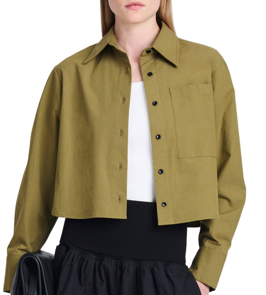 A person wearing a cropped olive-green button-up Proenza Schouler Alma Shirt in peached poplin over a white top, paired with a black skirt, and holding a black bag.