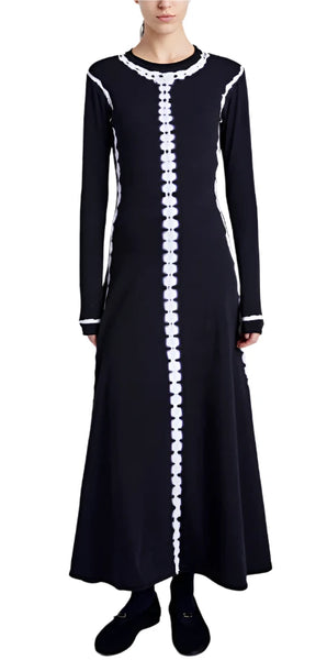 Back view of a person wearing the Proenza Schouler Kieran Tie Dye Dress, a long-sleeved black dress with white decorative trim down the center and along the sides, featuring an A-line silhouette and an ankle-grazing hem.