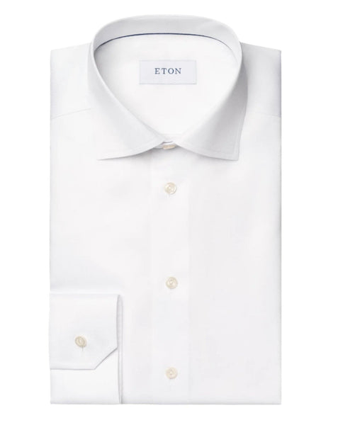 Eton's iconic Eton White Signature Twill Shirt, Contemporary Fit exudes timeless elegance with its folded white dress shirt featuring a spread collar, buttoned cuffs, and white buttons. The label "ETON" graces the inside of the collar, all set against a plain gray background. This wrinkle-free Signature Twill ensures both style and convenience.