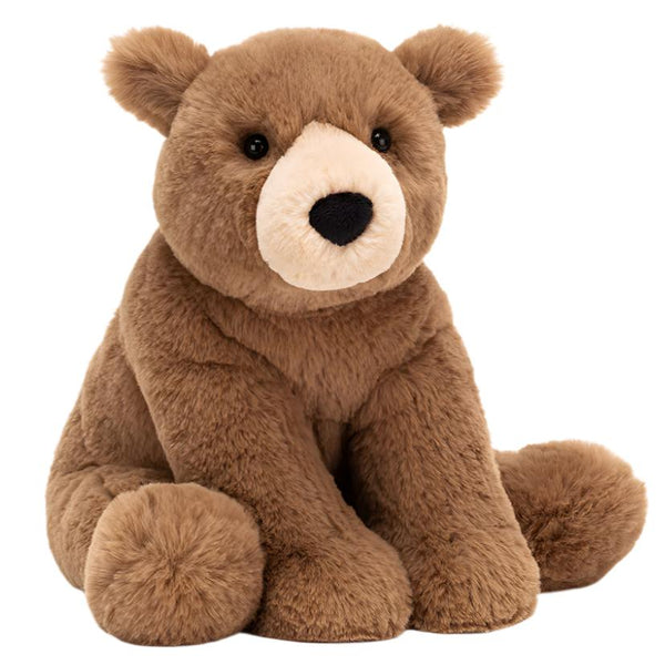 A Jellycat plush teddy bear, known as the Jellycat Woody Bear, features a rich brown coat with a lighter brown snout and black eyes, sitting upright against a white background.