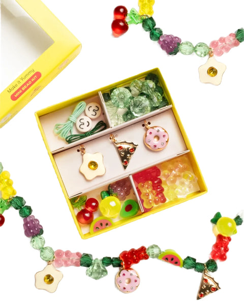 The Super Smalls Make It Yummy Mini Bead Kit by Super Smalls features a vibrant yellow craft box filled with colorful, faux-food beads and accessories, neatly organized in compartments. A partially completed beaded bracelet is displayed beside this creative jewelry kit, adding a burst of fun to your crafting experience.