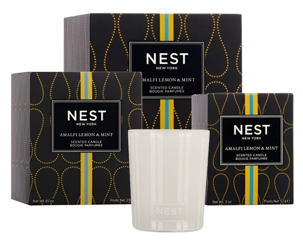 Three boxes of Nest's NEST Amalfi Lemon & Mint Collection candles sit behind the glass candle, reflecting the serene essence of the Amalfi Coast and creating a captivating sight.