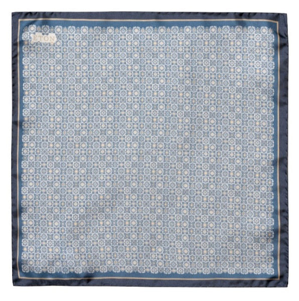 The Eton Navy Blue Medallion Twill Silk Pocket Square features a blue and white geometric pattern with a stylish blue border, making it an excellent accessory for business attire. The word "ETON" is elegantly printed in the top left corner.