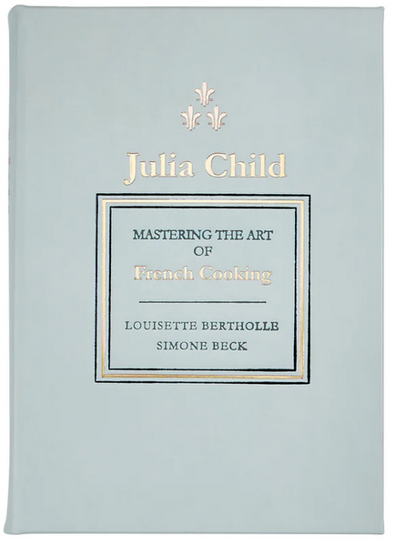 A light blue, leather-bound book cover titled "Mastering the Art of French Cooking Leather" by Graphic Image, the definitive cookbook on French cuisine by Julia Child, Louisette Bertholle, and Simone Beck, adorned with gold and black text.