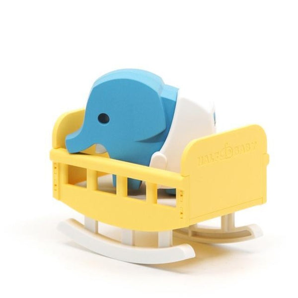 A small, blue Halftoys Babies elephant sits in a yellow rocking crib with white rockers, revealing its unique skeletal structure like a puzzle.