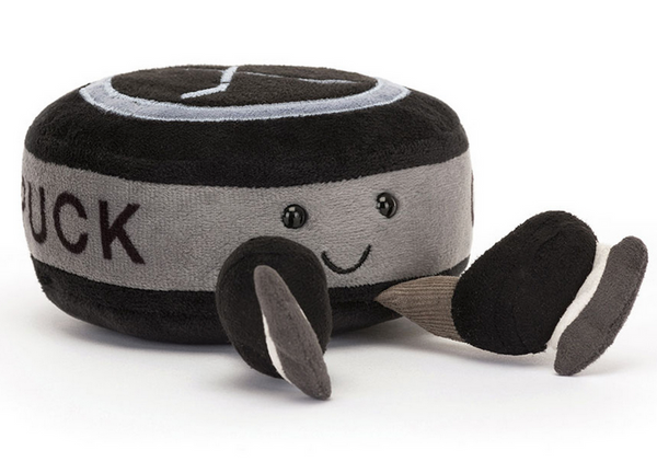 A Jellycat Amuseables Sports Ice Hockey Puck, a plush toy shaped like a hockey puck with soft black fur and a smiling face, complete with detachable, embroidered hockey stick accessories.