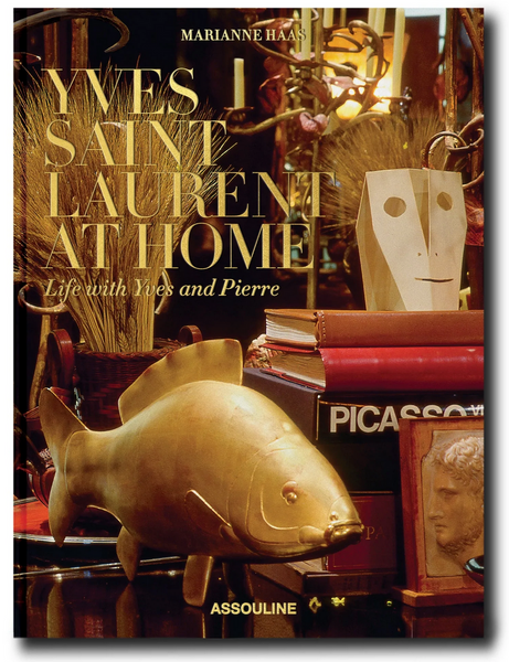 Cover of the book "Yves Saint Laurent at Home" by Assouline, showcasing an array of eclectic decor items such as a brass fish, a mask, and a Picasso book, all masterfully curated by the esteemed interior designer Jacques Grange.