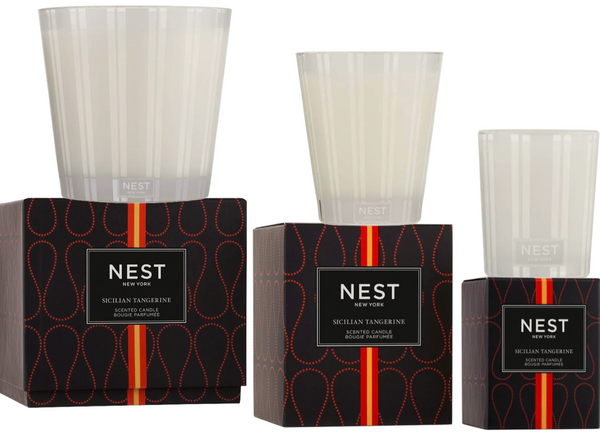 Two NEST Sicilian Tangerine candles from the Nest brand, each housed in a clear glass holder and positioned atop a black box featuring a red and orange design.