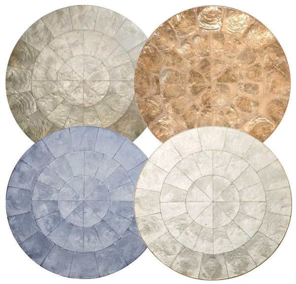 Four circular rugs, inspired by Kim Seybert Capiz Placemats, are arranged in a 2x2 grid. Each rug showcases a unique texture and color: silver, gold, blue, and cream. The design on each rug features a segmented sunburst pattern perfect for beach-inspired accessories.