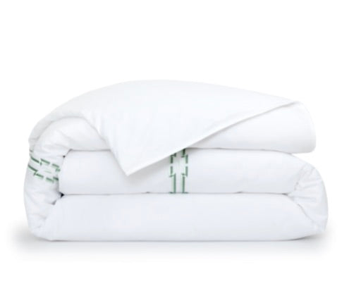 A neatly folded white comforter from the Yves Delorme Couture Tuileries Bedding Collection, with a corner portion slightly unfolded, displaying a hint of green geometric embroidery underneath.