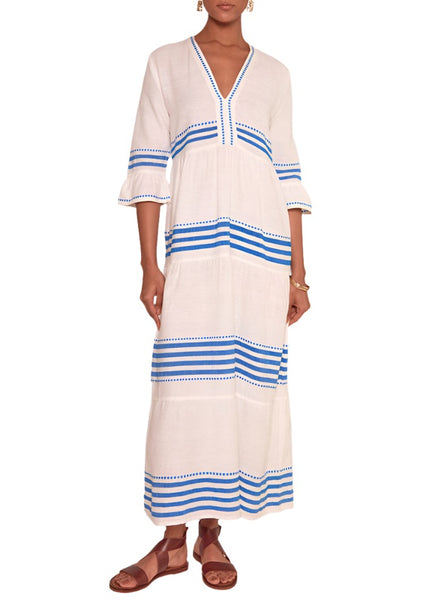 Person wearing a white lemlem Hawi Flutter Dress by Lemlem, with blue stripe accents, meticulously hand-woven in Ethiopia, paired with brown sandals.