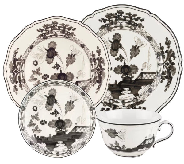 The GINORI 1735 Oriente Italiano Albus Collection by Ginori 1735 features a white porcelain dinnerware set adorned with black floral patterns, including a large plate, a medium plate, a small bowl, and a cup with a handle. Inspired by the elegance of the iconic Oriente Italiano collection, this set adds timeless charm to any table setting.