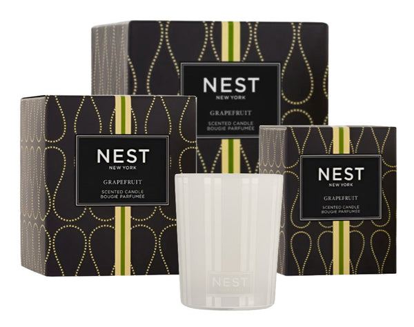 The NEST Grapefruit Candle Collection by Nest features three black boxes with gold and green accents next to a clear glass candle, exuding a refreshing grapefruit fragrance.