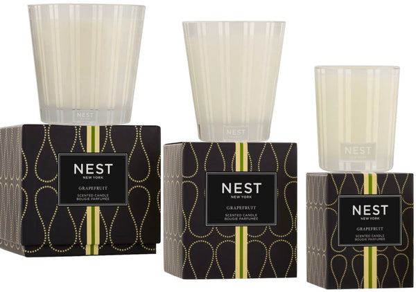 Three NEST Grapefruit Candle Collection scented candles by Nest are displayed. Each part of this exquisite candle collection is housed in frosted glass, with two set on black boxes featuring a gold and black geometric design. The refreshing fragrance lingers gracefully in the air, offering a touch of elegance to any space.