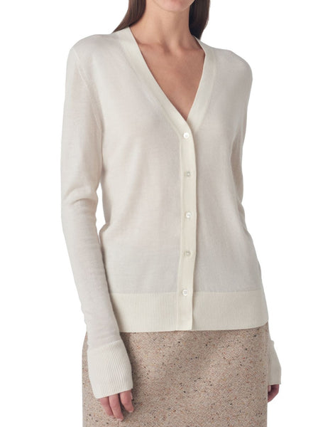 A person wears a versatile, light-colored CO V Neck Fine Cashmere Cardigan by CO over a textured skirt. The lightweight cardigan features long sleeves and a ribbed waist and cuffs.