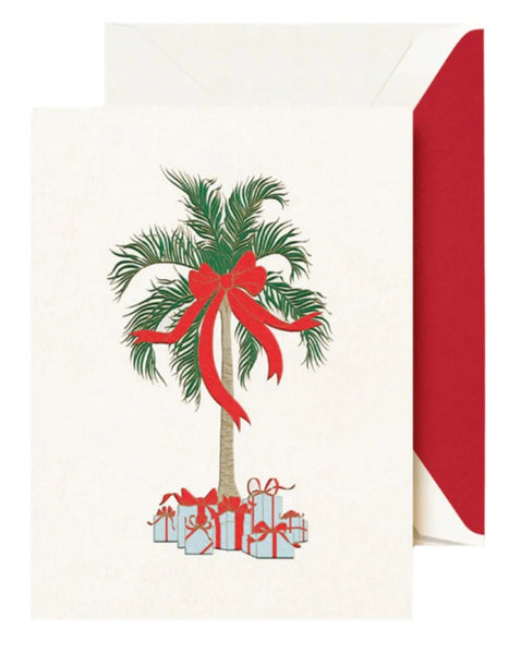 The Crane Christmas Palm Card Set by Crane showcases a beachy holiday card with a palm tree illustration adorned with a red ribbon and bow. Gifts wrapped in red ribbons are arranged at the base of the tree for an extra festive feel. This lively, tropical-themed card comes with an envelope featuring a red interior.