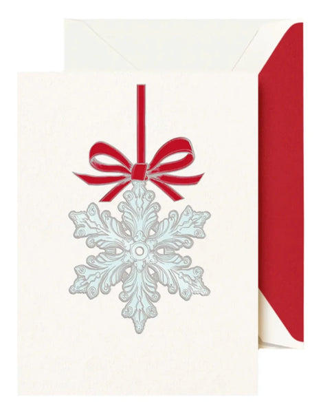 Crane's Snowflake Ornament Card Set showcases a holiday card adorned with a silver snowflake ornament and a red bow set against a crisp white background. Complementing the elegant design, an envelope lined with red peeks from behind, encapsulating the spirit of a winter wonderland.