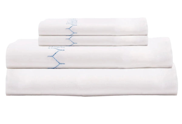 A neatly folded stack of white bedding sheets is displayed, with the top sheet featuring light indigo stitching reminiscent of the John Robshaw Stitched Light Indigo Sheet Set.