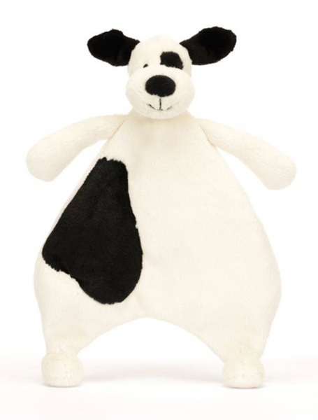 A Jellycat Bashful Black & Cream Puppy Comforter resembling a white and black dog with floppy ears, soft cream fur, and a spot over one eye is part of the Jellycat collection. It is crafted from recycled fibers to offer both comfort and sustainability.