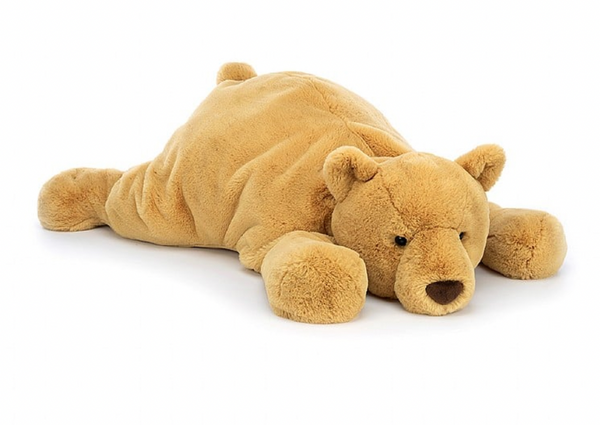 A plush teddy bear lies flat on its stomach with its head resting on its front paws against a white background. This adorable stuffed bear, lovingly named Jellycat Harvey Bear, exudes comfort and charm.