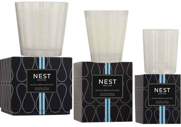 Two Nest Ocean Mist and Sea Salt Candle Collection candles in transparent glass jars, placed on top of their boxes with 'Coconut & Sea Salt' label. The left box has a lid with ocean mist patterns, while the right one does not.