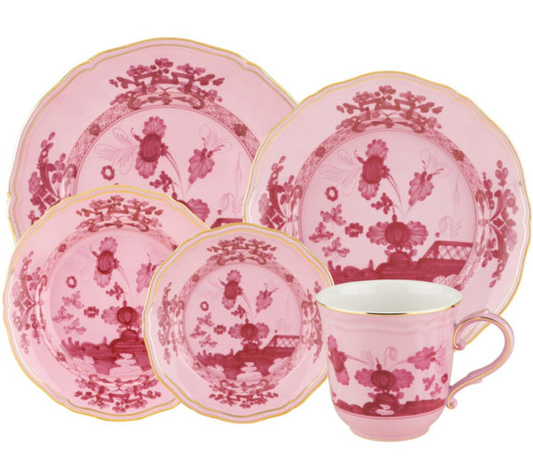 The GINORI 1735 Oriente Italiano Porpora Collection by Ginori 1735 features a stunning set of pink ceramic dinnerware adorned with intricate red floral patterns and gold trim detailing. This exquisite collection includes two plates, two bowls, and a cup with a handle, each piece embodying the exotic beauty reminiscent of Ginori 1735.