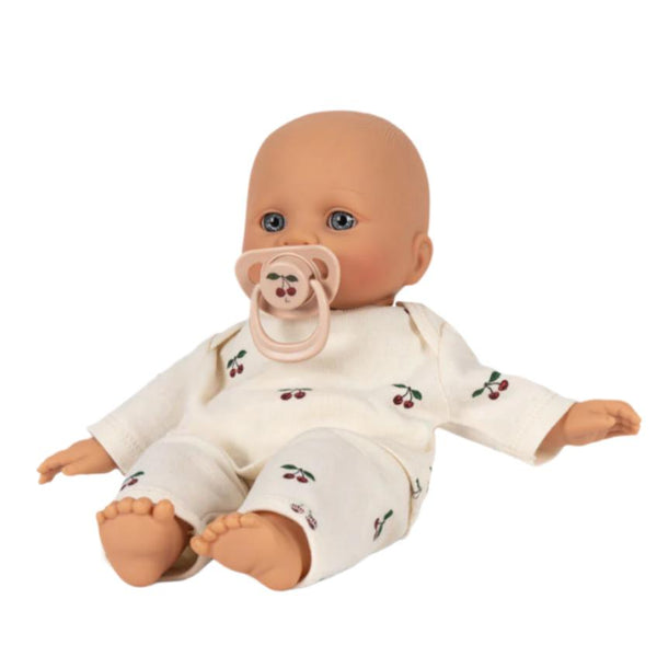 Konges Slojd's Elli the Doll is a vinyl figure wearing white pajamas adorned with cherry patterns, crafted from organic cotton, and features a pacifier in its mouth while seated upright.