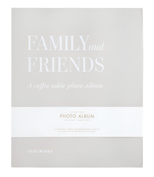 A photo album with a grey cover titled "PrintWorks Family and Friends Photo Album" features a white band around the middle with additional text, crafted to offer a stylish and convenient photo display using high-quality black photo paper.