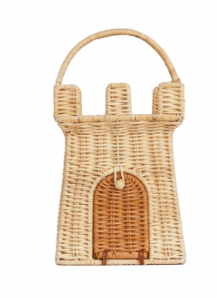 The Olli Ella Rattan Castle Bag by Olli Ella is a handwoven basket shaped like a small fortress, featuring a curved handle on top and an arched opening at the bottom center, reminiscent of a castle drawbridge.