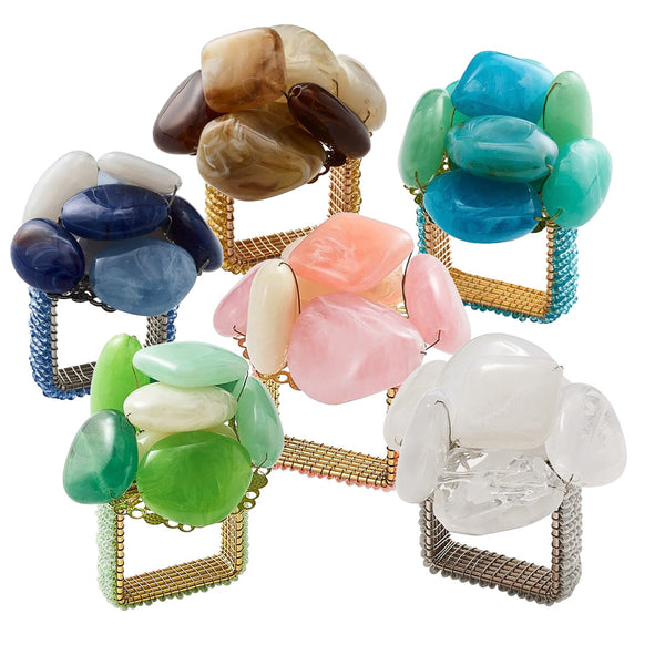 A set of six Kim Seybert Sea Stone Napkin Rings in assorted colors, showcasing clusters of polished and cream resin stones on square woven metal bases.