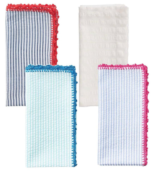 The Kim Seybert Seersucker Napkin Set (set of 4) by Kim Seybert includes four colorful folded fabric napkins featuring a mix of textured and striped patterns. Three napkins boast scalloped edges in vibrant red, pink, and blue hues, while the fourth is a plain white cotton napkin.