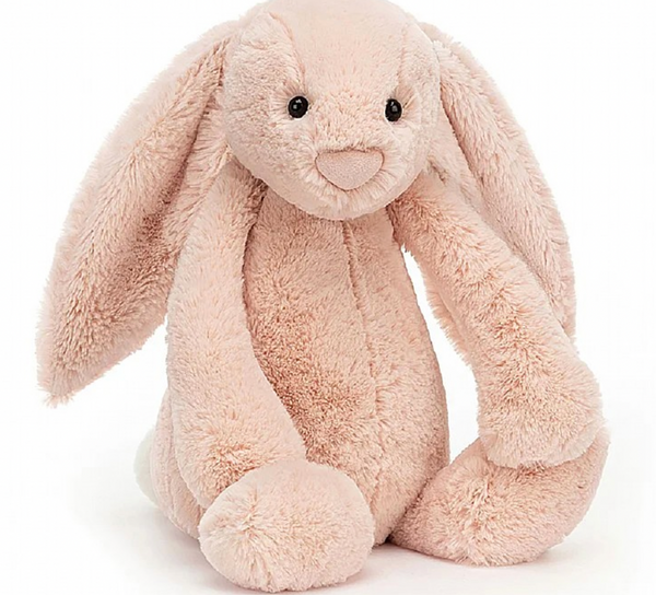 The Jellycat Bashful Blush Bunny, Huge, with its super soft peachy fur, long floppy ears, and black eyes, is shown sitting upright. This plush, light pink bunny from Jellycat is the perfect cuddle buddy.