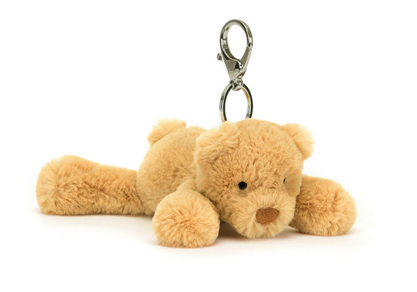 A small, plush teddy bear keychain with a metal clasp, tagged with a signature Jellycat tag. The light brown bear lies flat, making it a perfect Jellycat Smudge Bear Bag Charm or soft plush toy accessory.